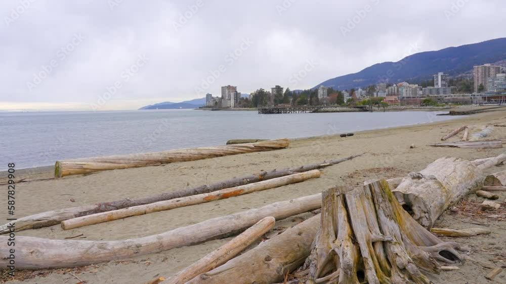Establishing shot of ocean beach with rocks, pebbles and wood logs in slow motion at summer day in Vancouver, Canada, North America. Day time on September 2022. Still camera. ProRes 422 HQ. Establishing shot of ocean beach with rocks, pebbles and wood logs in slow motion at summer day in Vancouver, Canada, North America. Day time on September 2022. Still camera. ProRes 422 HQ.