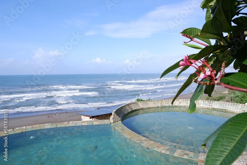 Fresh cool blue pool and ocean waves with infinity view of clear sky background with stairs pool ,wooden chair tree leaves in Parang Tritis beach Yogyakarta, Indonesia