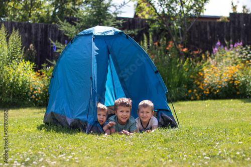 Three little boys lie in a blue tourist tent in the yard. 