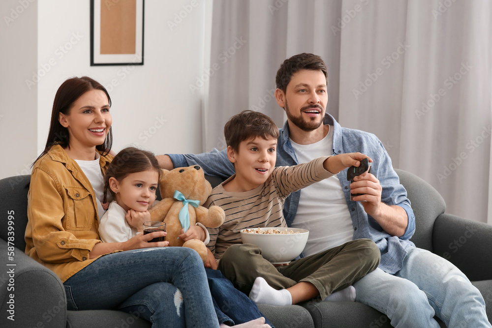 Happy family watching TV at home. Son changing channels with remote control Happy family watching TV at home. Son changing channels with remote control