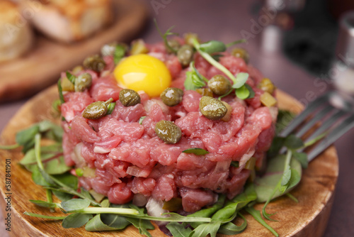 Tasty beef steak tartare served yolk, capers and microgreens on serving board, closeup