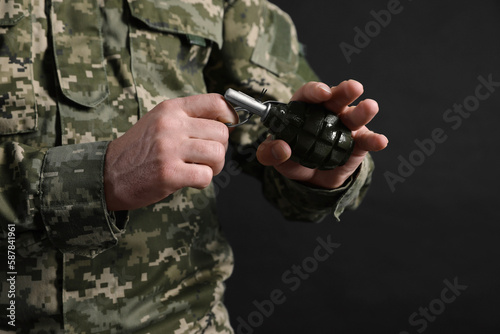 Soldier pulling safety pin out of hand grenade on black background, closeup. Military service