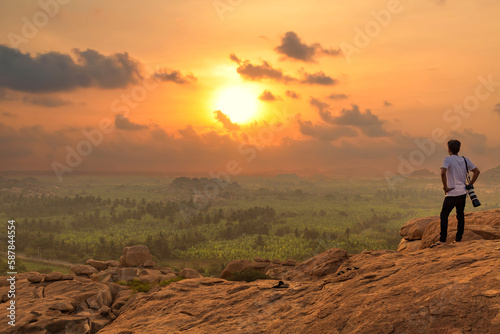 Male tourist photographer enjoys a scenic sunset view from a hill top at Hampi, Karnataka, India