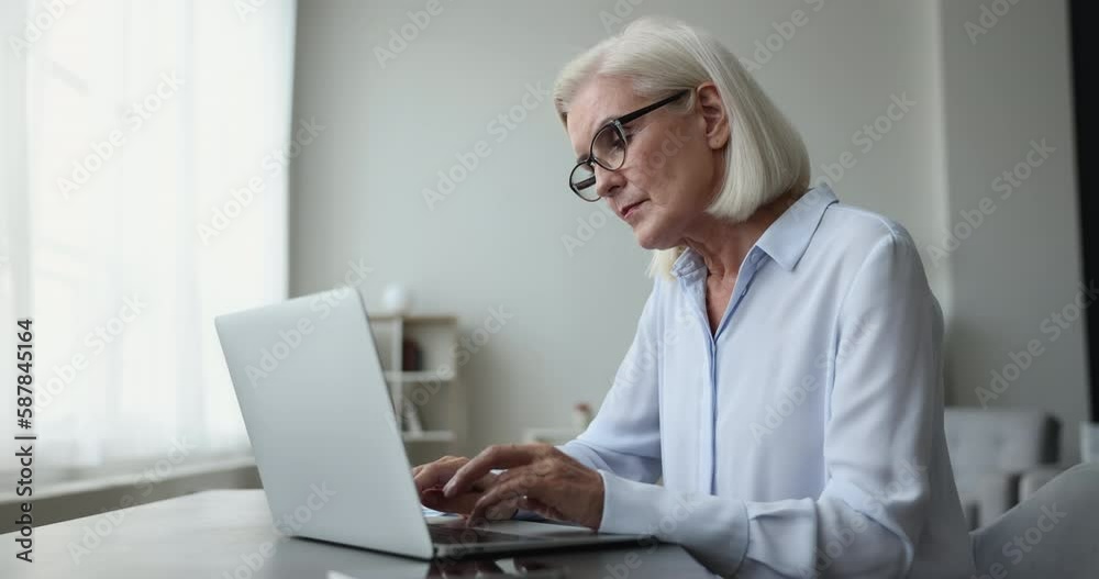 Pensive woman use laptop engaged in on-line workflow. Older businesswoman in glasses sit at desk, typing on computer looks focused, search solution, learn e-mail, ponders over answer to client, thinks Pensive woman use laptop engaged in on-line workflow. Older businesswoman in glasses sit at desk, typing on computer looks focused, search solution, learn e-mail, ponders over answer to client, thinks