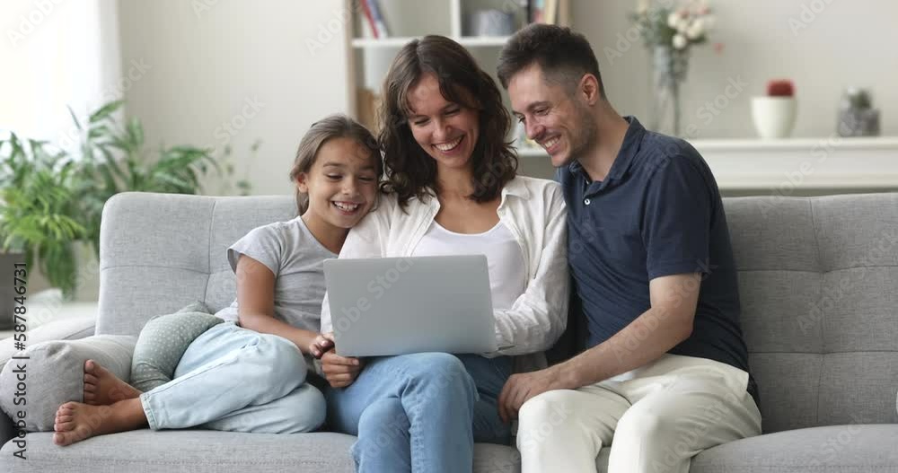 Happy Hispanic couple and little cute daughter resting together on couch watch funny videos, movie on-line, spend pastime on internet use laptop. Family leisure at home with modern wireless technology Happy Hispanic couple and little cute daughter resting together on couch watch funny videos, movie on-line, spend pastime on internet use laptop. Family leisure at home with modern wireless technology