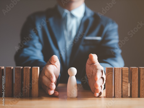 Risk management and assessment concept. Businessman prevent or protect his business and employee from high risk. Wood block represent of risk attack to business, two hands block and protect the domino photo