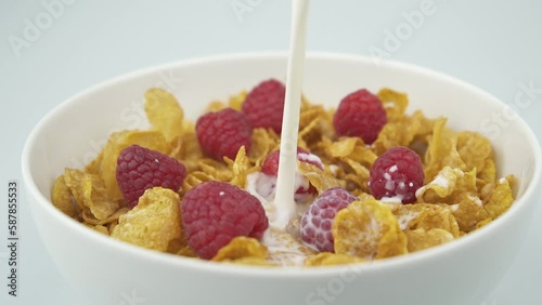 Pouring milk on corn flakes with raspberries