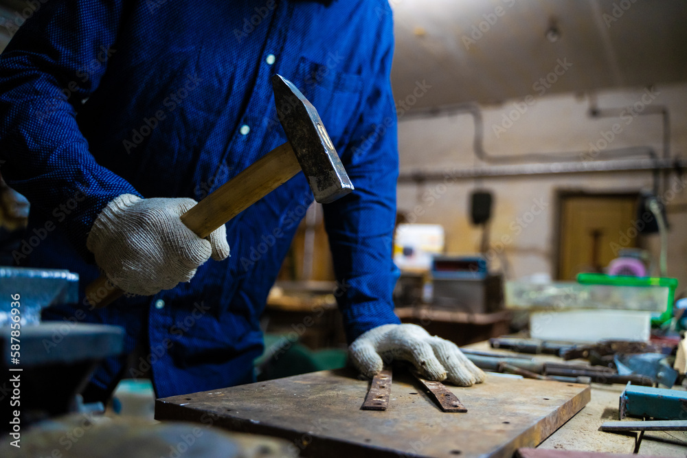 A man works with a hammer in a workshop.