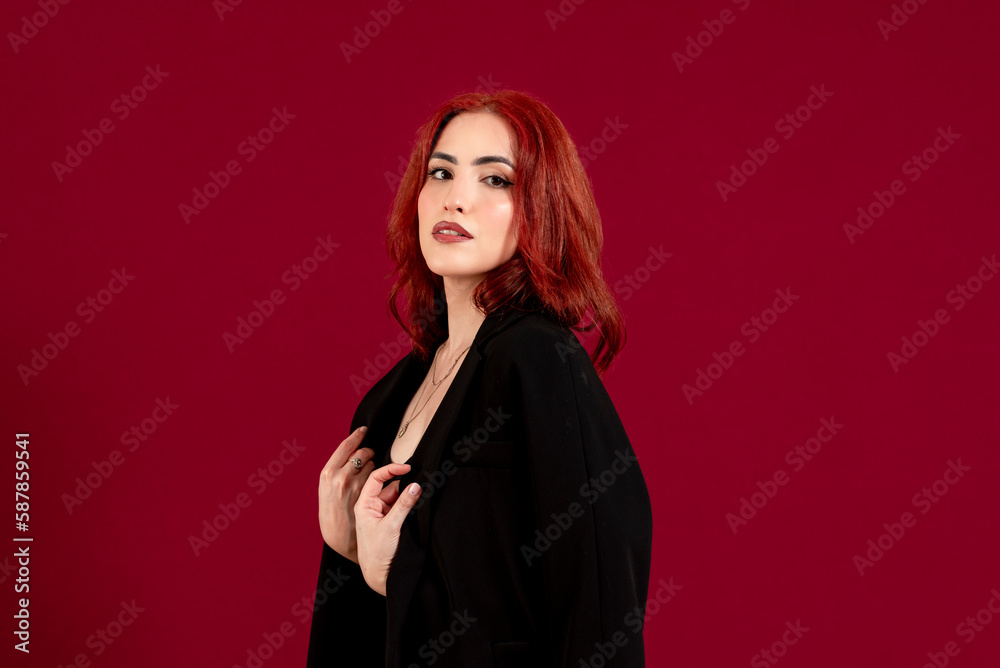Confident woman looking at the camera and smiling while posing against a red isolated background. Confident woman looking at the camera and smiling while posing against a red isolated background.