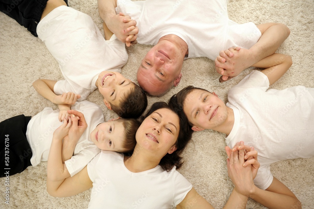Happy family concept. Top view happy family five tied to each other and smiling, lying on a wooden floor with a carpet. Caucasian large family in the living room on a warm floor. High quality photo