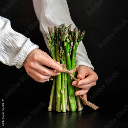 Person holding bunch of asparagus on black background