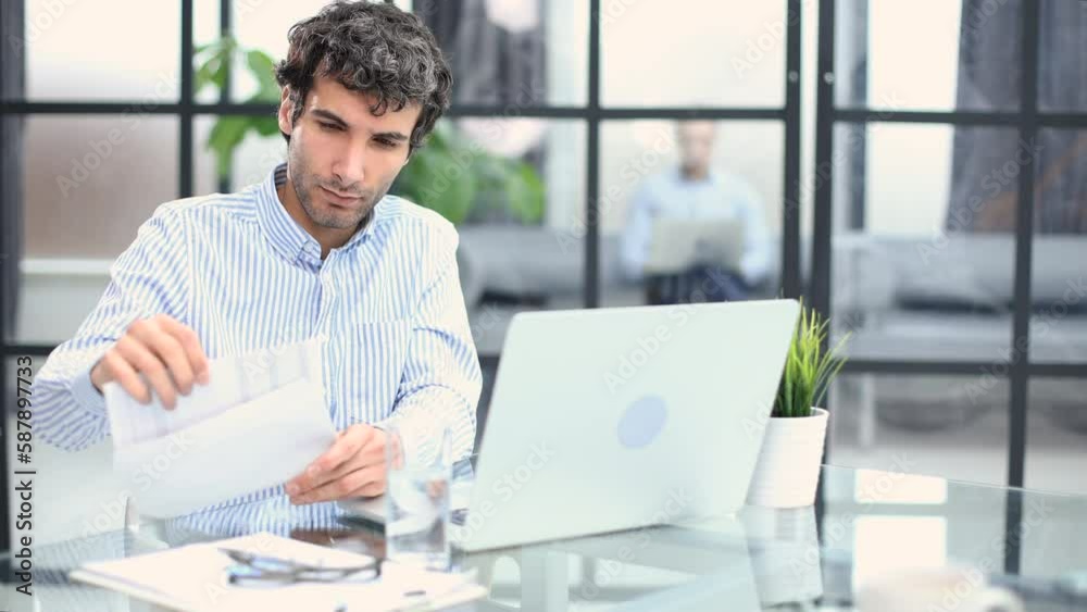 Entrepreneur opening an envelope in a desktop at office. Collegue is on the background.
