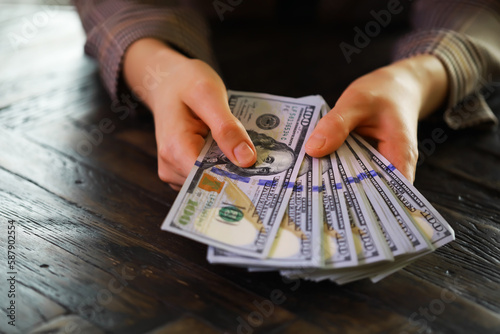 Female hands counting American one hundred dollar bills against the background of smaller bills of money lying on the table