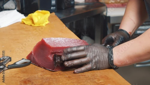 Close-up of the process of cutting tuna fish at the market. Male hands in gloves cutting a large fish with a knife.