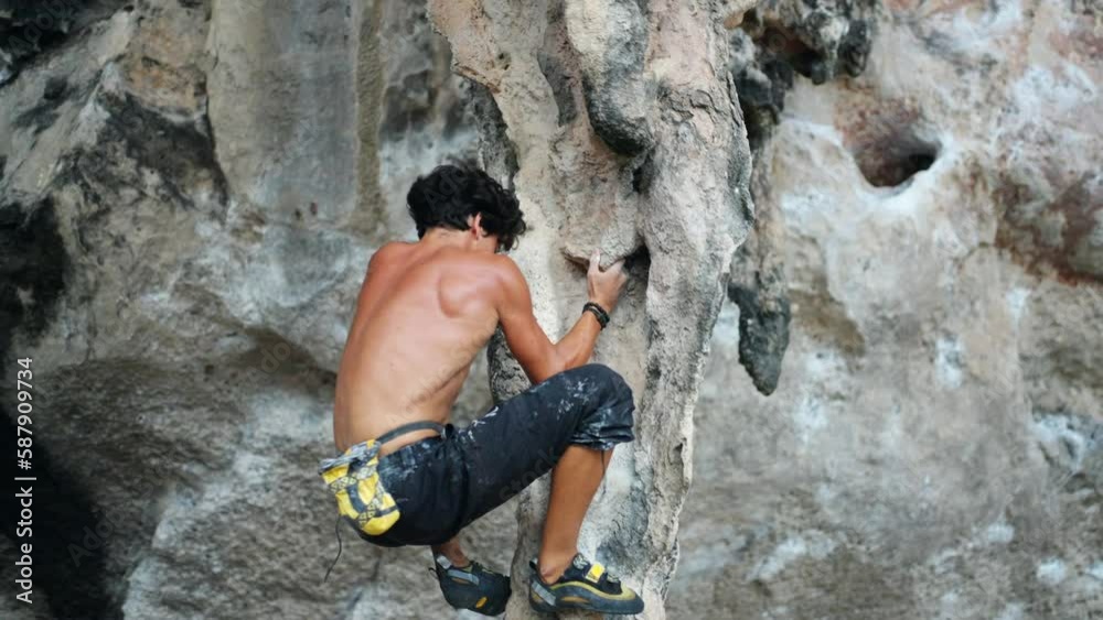 Young Asian man climber climbing on rocky coastline at tropical island in sunny day. Handsome guy enjoy outdoor active lifestyle and extreme sport training mountain climbing on summer holiday vacation