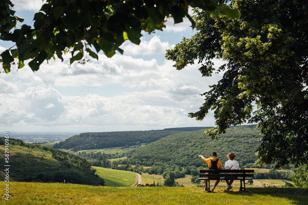 Un couple assis sur un banc admirant un paysage de Bourgogne. Des touristes sur un banc regardant le paysage. A l'ombre d'un arbre, un couple se repose face à un panorama. Un couple assis sur un banc admirant un paysage de Bourgogne. Des touristes sur un banc regardant le paysage. A l'ombre d'un arbre, un couple se repose face à un panorama.