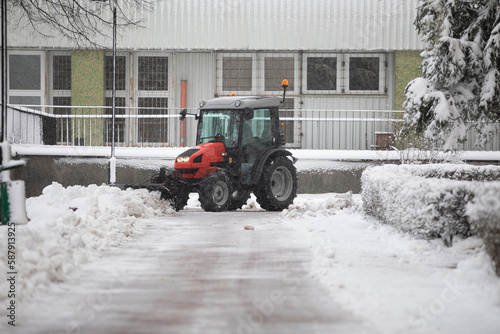 A vehicle equipped with snow removal equipment stands in front of the building