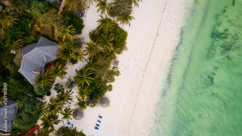 A gorgeous tropical beach with white sand, palm trees, turquoise ocean against a blue sky with clouds on a sunny summer day. The perfect backdrop for a relaxing vacation, Zanzibar Island.