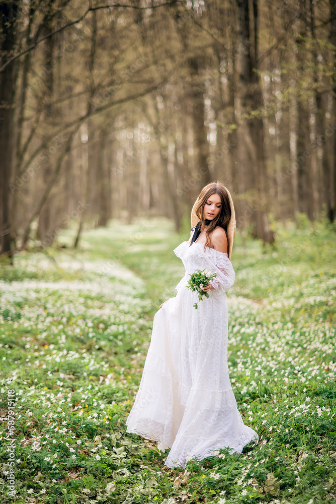 girl in a white long dress in a spring forest. Forest fairy with a bouquet of primroses