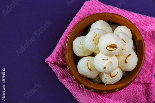 Indian Sweet or Dessert - Rasgulla, Famous Bengali sweet in clay bowl with blue napkin on violet background photo