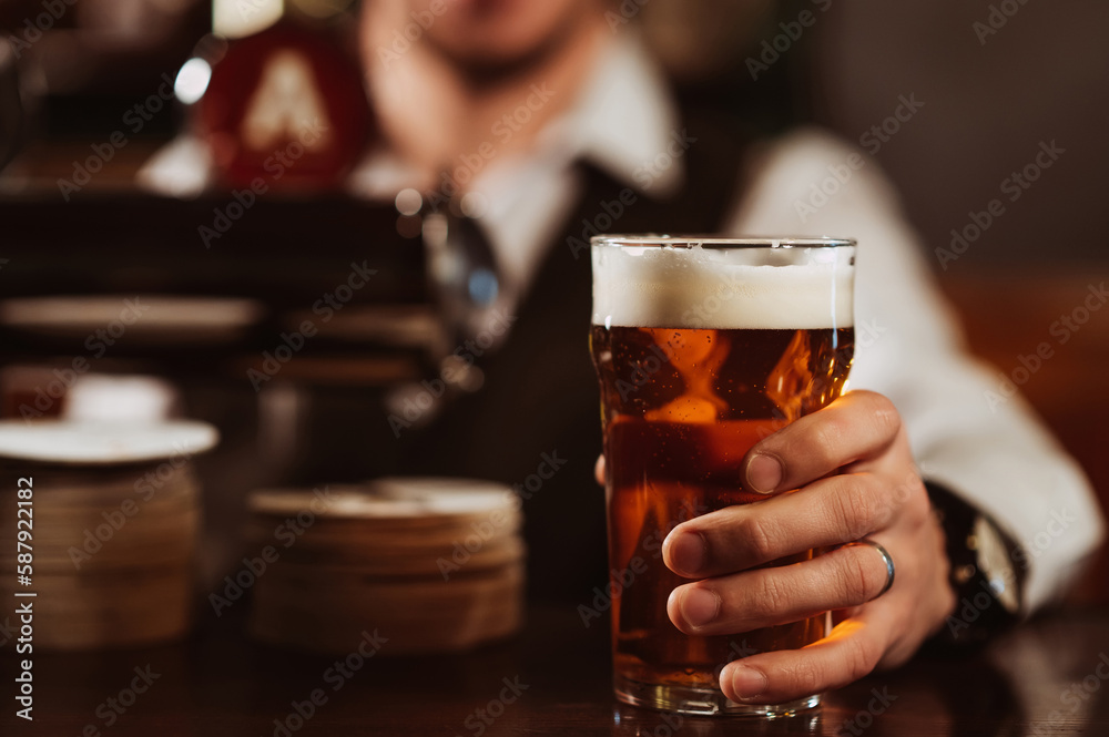 bartender's hand with a glass of light draft beer with foam in bar close-up