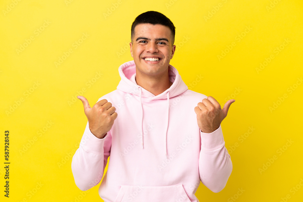 Young handsome man over isolated yellow background with thumbs up gesture and smiling