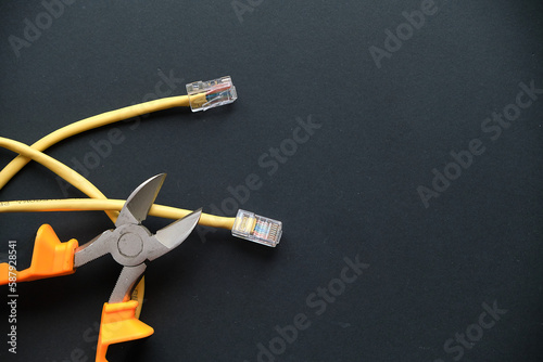 pliers and yellow internet cable on a black background. the concept of turning off wired internet for non-payment.