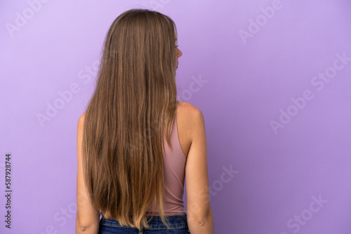 Young Lithuanian woman isolated on purple background in back position and looking side