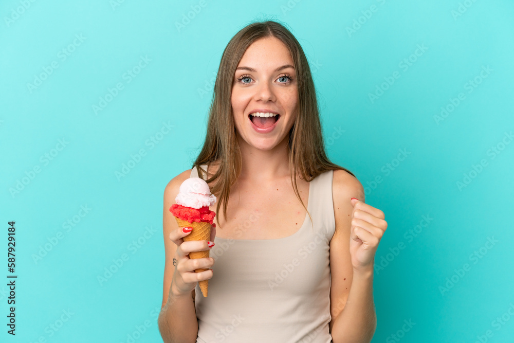 Young Lithuanian woman with cornet ice cream isolated on blue background celebrating a victory in winner position Young Lithuanian woman with cornet ice cream isolated on blue background celebrating a victory in winner position