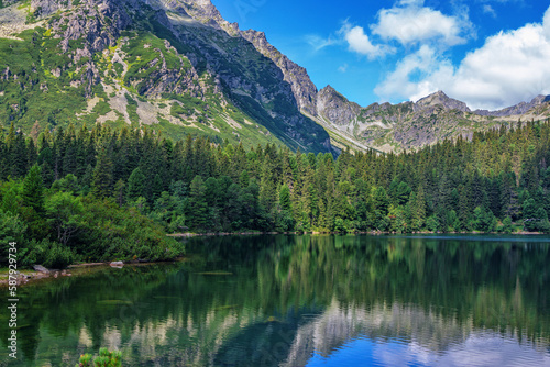 Beautiful summer landscape of High Tatras  Slovakia - Poprad lake  lush forest  reflecting on water surface  mountains and white clouds on the sky