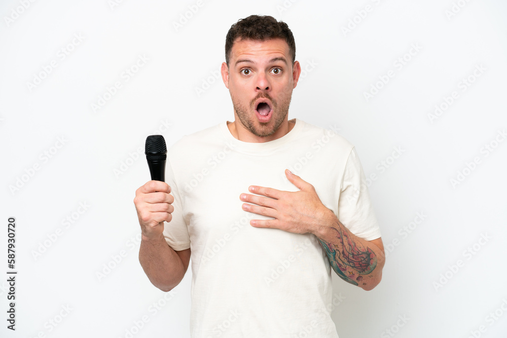 Young caucasian singer man picking up a microphone isolated on white background surprised and shocked while looking right Young caucasian singer man picking up a microphone isolated on white background surprised and shocked while looking right