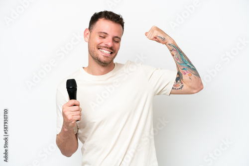 Young caucasian singer man picking up a microphone isolated on white background doing strong gesture