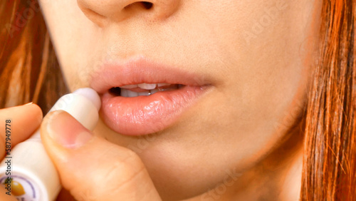 Close-up of the lips of a pretty young woman smearing them with lip balm