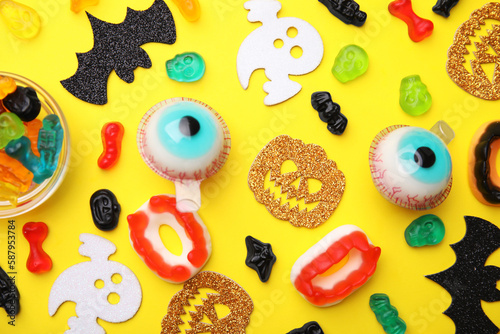 Tasty colorful jelly candies and Halloween decorations on yellow background, flat lay