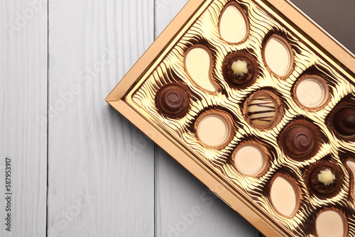 Partially empty box of chocolate candies on white wooden table, top view. Space for text