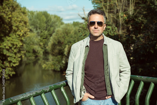 Middle-aged man with sunglasses posing at the river beach, autumn outdoor portrait. Handsome mature man. Outdoor male portrait.