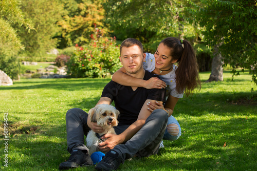 Young couple with puppy. Portrait of attractive happy smiling young woman and man holding cute little dog, summer park outdoor.