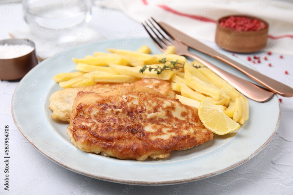 Tasty soda water battered fish, potato chips and lemon slice served on white textured table Tasty soda water battered fish, potato chips and lemon slice served on white textured table