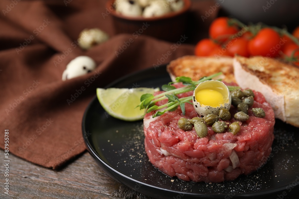 Tasty beef steak tartare served with quail egg and other accompaniments on wooden table, closeup