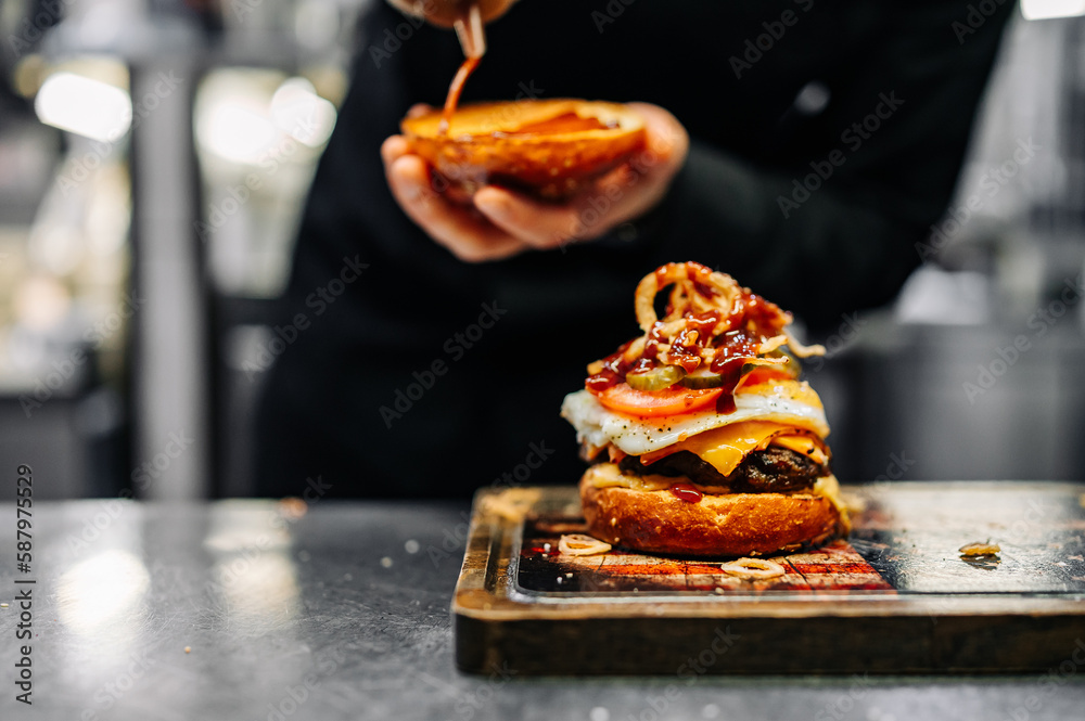 chef hand cooking cheeseburger with vegetables and egg on restaurant kitchen