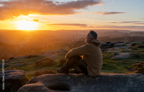 man in special boots walking in the mountains with bag of dron reaching the destination and on the top of mountain in Peak District at sunset on autumn day Travel Lifestyle concept