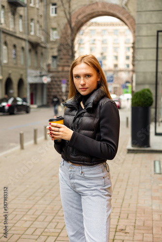 Young woman in black jacket and jeans with coffee on the street urban fashion