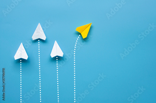 Yellow paper plane leaving other white airplanes on blue background.