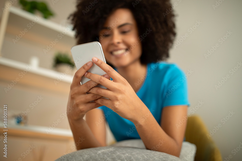 Cheerful millennial african american curly lady typing on smartphone, watch video, read message Cheerful millennial african american curly lady typing on smartphone, watch video, read message
