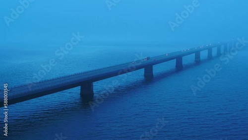 Aerial of traffic over the bridge Storebæltsbroen in Denmark. There is a heavy fog, and it is during the blue hour. 4K photo