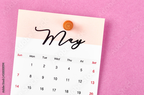 A May 2023 calendar and wooden push pin on pink colour background.