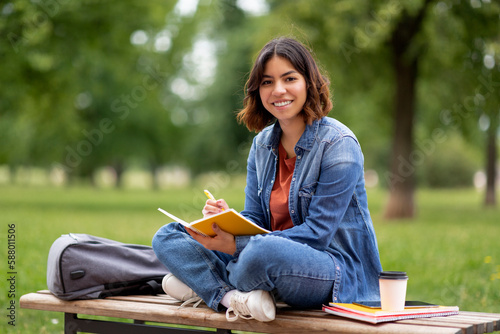 Young middle eastern woman writing in notebook while sitting on bench outdoors photo