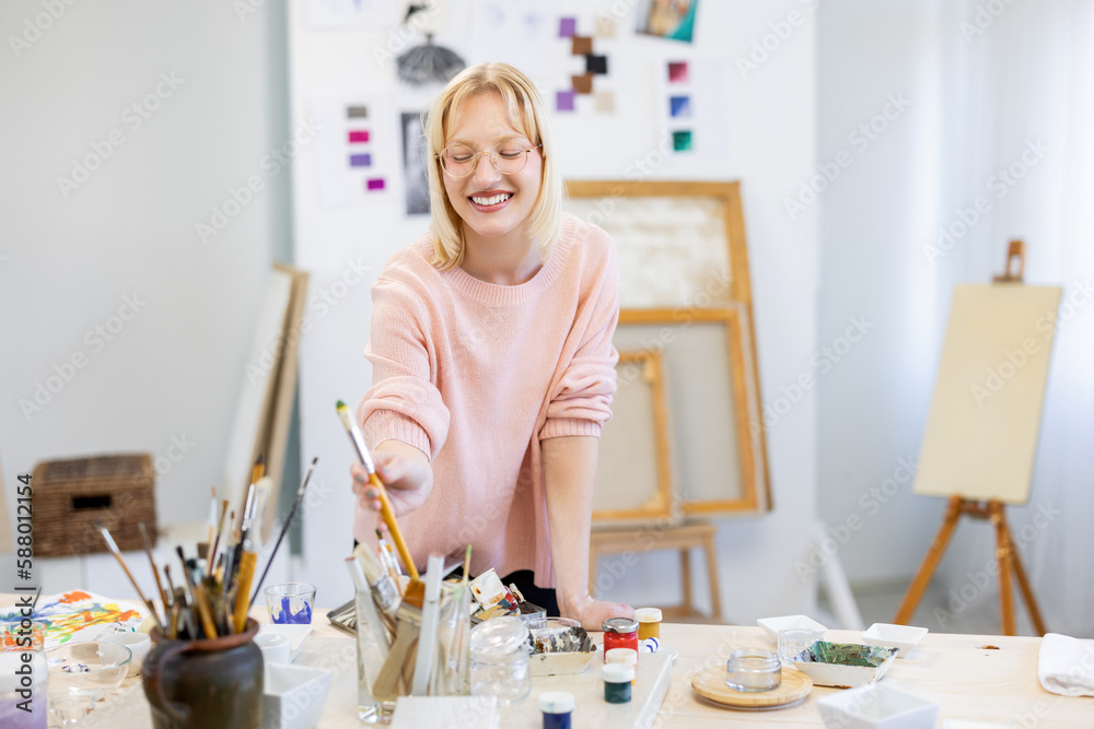 Young woman is in her painting studio. She is smiling for the camera in front of her working table Young woman is in her painting studio. She is smiling for the camera in front of her working table