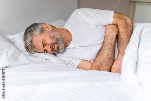 Middle aged man lying in bed, suffering from stomach pain