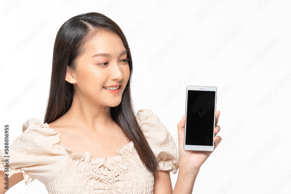 Happy attractive asian young woman smile and showing mobile phone isolated on white background. Cheerful pretty girl wear casual dress raise up smartphone to empty space for mockup to display product Happy attractive asian young woman smile and showing mobile phone isolated on white background. Cheerful pretty girl wear casual dress raise up smartphone to empty space for mockup to display product
